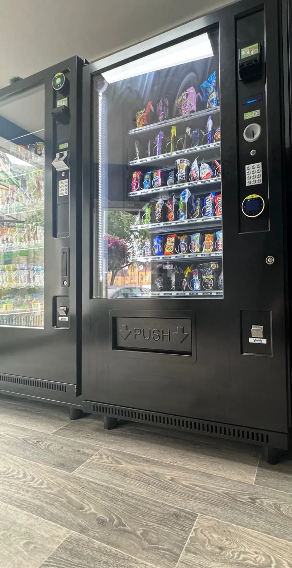 Zwei schwarze Snackautomaten mit Kartenzahlung, gut gefüllt mit Riegeln und Chips